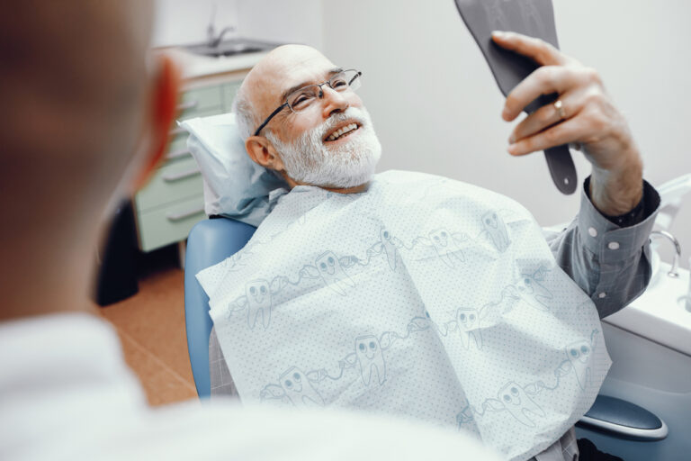 Handsome old man looking into the mirror on his teeth